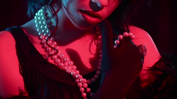 Woman dressed in style of Great Gatsby wearing pearl beads and black feathers boa. Neon blue and red light. Roaring twenties, retro, party, fashion concept — Stock Video