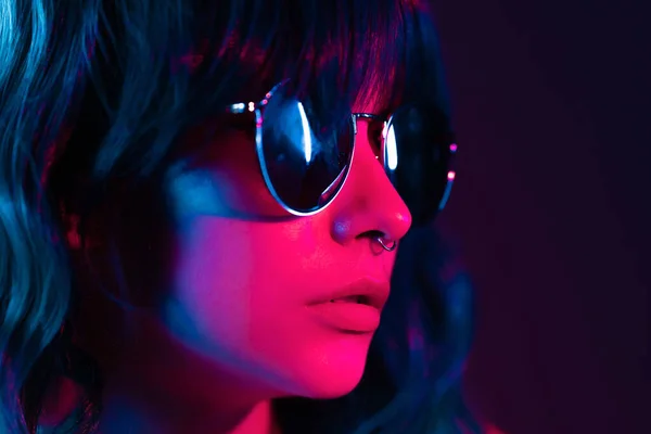 Portrait of alluring blue haired girl in pink neon light. Fashion, glamour, model concept. Seductive woman with make-up and sunglasses posing in dark room at night — Stock Photo, Image