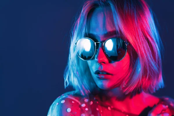 Close up portrait of millennial pretty girl with short hairstyle with neon light. Dyed blue and pink hair. Mysterious hipster teenager in glasses. — Stock Photo, Image