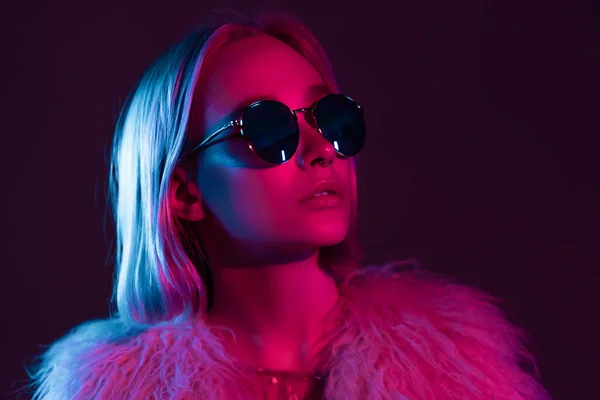 Close up portrait of millennial pretty glamour girl in fluffy fur coat in neon light. Dyed blue and pink hair. Mysterious hipster teenager in glasses. — Stock Photo, Image