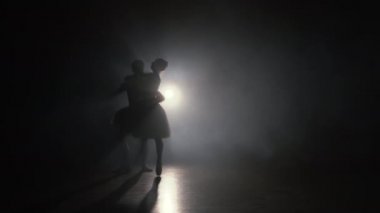 Romantik profesyonel bale çifti karanlık sahnede dans ediyor. Klasik elbiseler içinde dans eden, etrafında dönüp gülümseyen genç bir çift. Her harekette zarafet ve şefkat..
