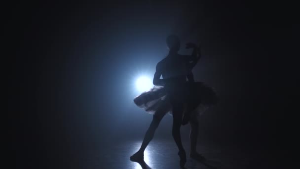 Egy fiatal férfi sziluettje, aki balett piruettben gyakorol balerinával a sötét füst stúdióban reflektorfényekkel. Az érzéki párok táncolnak. Lassú mozgás.. — Stock videók