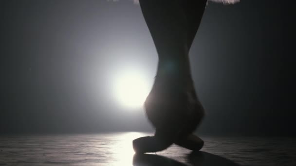 Primer plano de bailarina de ballet mientras practica ejercicios en un escenario o estudio oscuro. Mujeres pies en zapatos puntiagudos. Bailarina muestra pasos clásicos de ballet. En cámara lenta. Disparo de bengala . — Vídeos de Stock