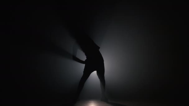 Silueta mladého muže, který se zahřívá před tréninkem v tmavém studiu s kouřem. Cvičení v tělocvičně, posilovna cvičení, 4k zpomalení — Stock video