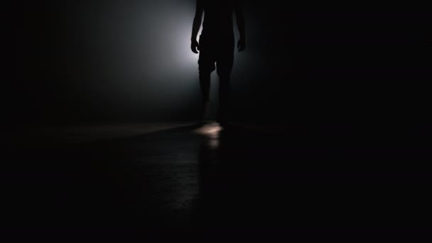 Sylwetka nogi młodego człowieka w sporcie nosić chodzenie przez dymne studio lub scena bezpośrednio do kamery. Podświetlenie, jasne światło reflektorów na tle. — Wideo stockowe