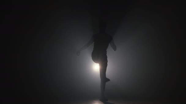 Egy fiatal férfi sziluettje, aki bemelegít, mielőtt a sötét stúdióban edz füsttel. Edzés tornateremben, erőnléti edzés, 4k lassított felvétel — Stock videók