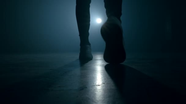 Silhouette of young man legs in sports shoes sneakers is walking through smoky studio or scene right from camera. Backlight, bright spotlight on background. — Stock Video