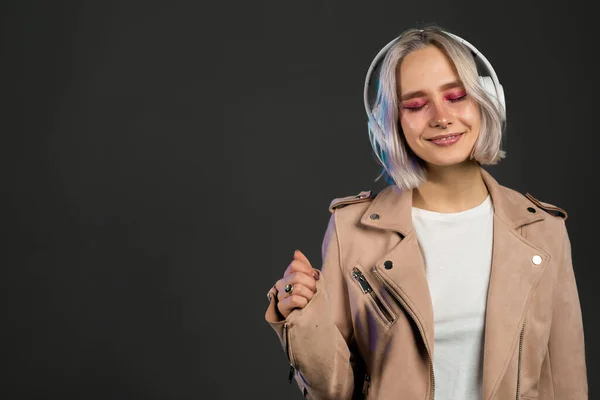 Okouzlující hipster teenager v růžové bundě, poslouchající hudbu se sluchátky. Portrét tisícileté hezké dívky s krátkým účesem. Kopírovat prostor — Stock fotografie