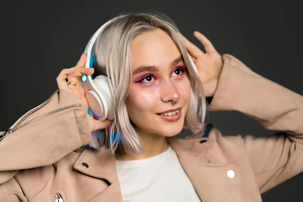 Záhadný hipsterský teenager poslouchající hudbu se sluchátky. Portrét tisícileté hezké dívky s krátkým účesem na šedém pozadí. Barvené vlasy. — Stock fotografie