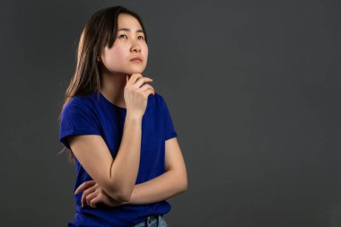 Gri arka planda etrafı kolaçan eden bir kadın. Dalgın yüz ifadeleri için endişelenmiş. Beyaz kapüşonlu güzel Asyalı kız modeli. Boşluğu kopyala