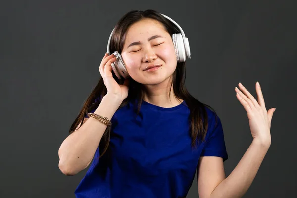 Junge schöne asiatische Frau mit Kopfhörern in moderner Kleidung genießt und tanzt auf grauem Hintergrund. Radio, Melodie, Technologiekonzept. — Stockfoto