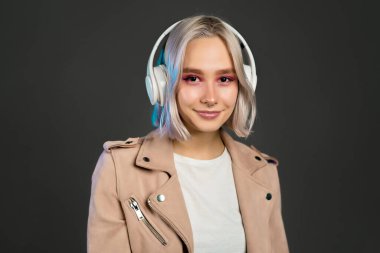 Gizemli hippi ergen kulaklıkla müzik dinliyor. Gri arka planda kısa saç stili olan bin yıllık güzel bir kızın portresi. Boyalı saç..