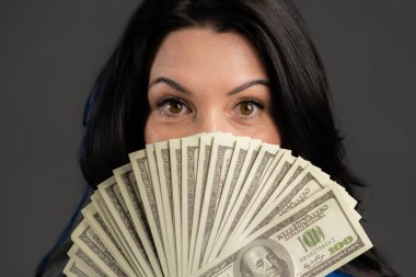 Gri duvarda Amerikan doları banknotları gösteren mutlu ve heyecanlı yetişkin kadın. Başarı, kazanç, zafer sembolü.