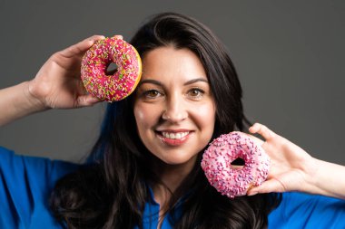 Gri stüdyo arka planında izole edilmiş renkli çöreklerle dans eden neşeli güzel bir kadının portresi. Neşe, yemek, yaşam tarzı kavramı.