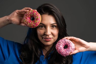 Gri stüdyo arka planında izole edilmiş renkli çöreklerle dans eden neşeli güzel bir kadının portresi. Neşe, yemek, yaşam tarzı kavramı.