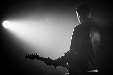 Deri ceketli rock gitaristi sırtını dumanlı stüdyoda ya da sahnede ustaca elektro gitar çalıyor. Sahne ışıkları altında tanınmayan bir müzisyenin görüntüsü.
