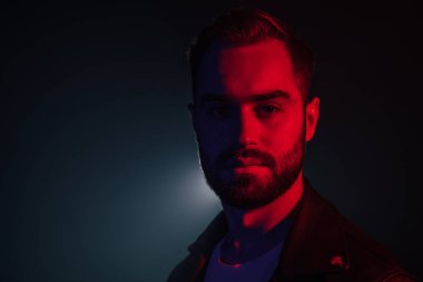 Deri ceketli, sakallı beyaz bir adamın portresi. Işığı aydınlatılmış, kameraya bakıyor. Esmer duman stüdyosu.
