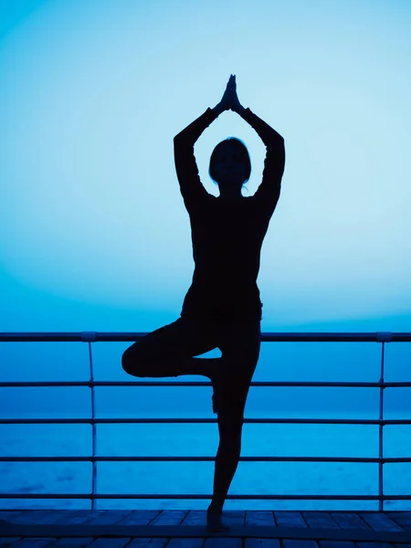 Young slim girl practicing yoga on embankment against ocean or sea at night time. Silhouette of woman in asana of tree. sleepwalking concept — Stock Photo, Image