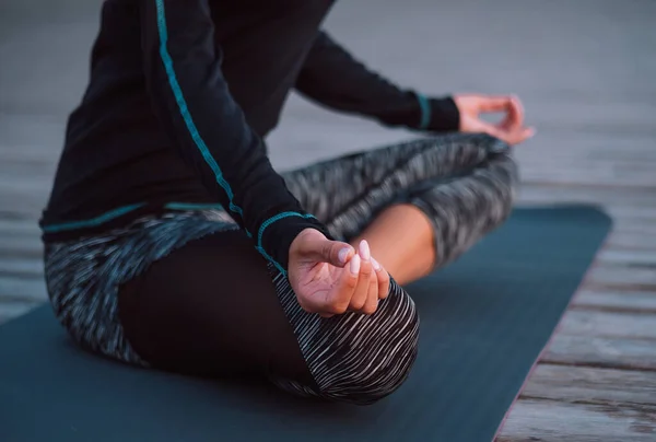 Невпізнавана концентрована жінка в чорному практикує медитацію йоги на дерев'яному узбережжі. Жінка в позі лотоса. Розтягування, практика, концепція здорового способу життя . — стокове фото