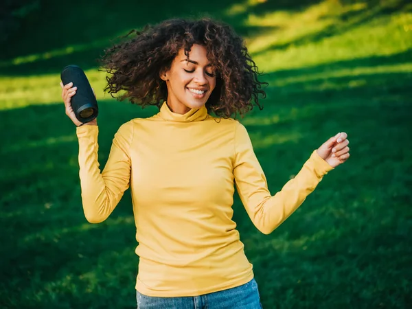 Modern moda Afrikalı Amerikalı kız kablosuz taşınabilir hoparlörden müzik dinliyor. Genç, güzel bir kadın eğleniyor, parkta dans ediyor.. — Stok fotoğraf