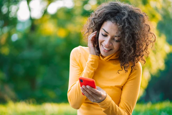 African woman using mobile phone over green background. Girl with curly hairstyle holding smartphone. Black female using technology.