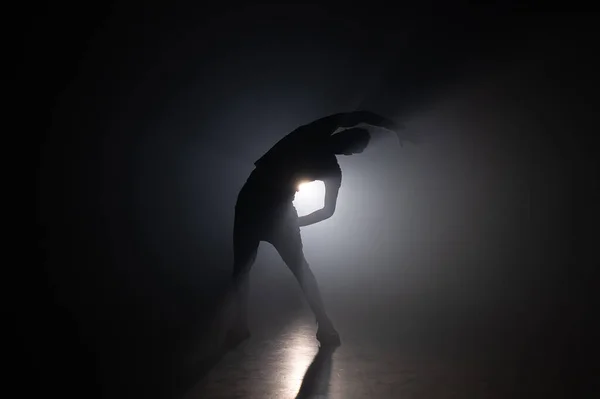 Silhouet van een jonge man die opwarmt voor hij in een donkere studio met rook traint. Trainen in de sportschool, krachttraining. — Stockfoto