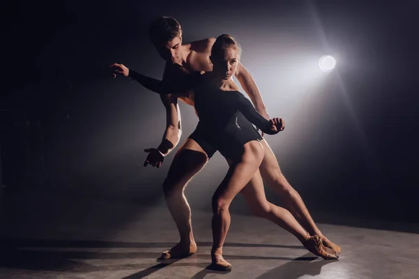 Prachtige jonge acrobaten of turners op een achtergrond van schijnwerpers. Professionele ballet paar dansen in schijnwerpers rook op groot podium. Emotioneel duet vertolkende choreografische kunst — Stockfoto