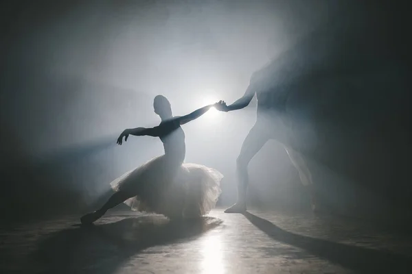Kecses balerina és férfi partnere táncoló elemei klasszikus vagy modern balett sötétben reflektorfényben. Egy pár füstöl fekete háttérrel. Művészeti koncepció. — Stock Fotó