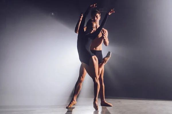 Prachtige jonge acrobaten of turners op een achtergrond van schijnwerpers. Professionele ballet paar dansen in schijnwerpers rook op groot podium. Emotioneel duet vertolkende choreografische kunst — Stockfoto