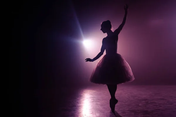 Balletttänzerin im Tutu, die auf die Bühne springt. Ballerina übt auf dem Fußboden in einem dunklen Studio mit Rauch. Veilchenlicht. — Stockfoto