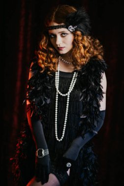 Great Gatsby dönemi tarzı giyinmiş eski moda kızıl saçlı kadın portresi bacaklarını gösteriyor ve naylon örgü çoraplarını ayarlıyor. Vintage, flapper party, retro moda konsepti