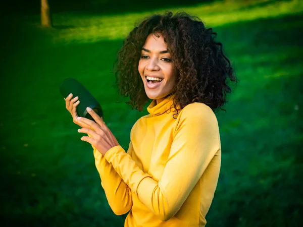 Moderne trendige afrikanisch-amerikanische Mädchen Musik hören durch drahtlose tragbare Lautsprecher.junge schöne Frau genießen, tanzen im Park. — Stockfoto