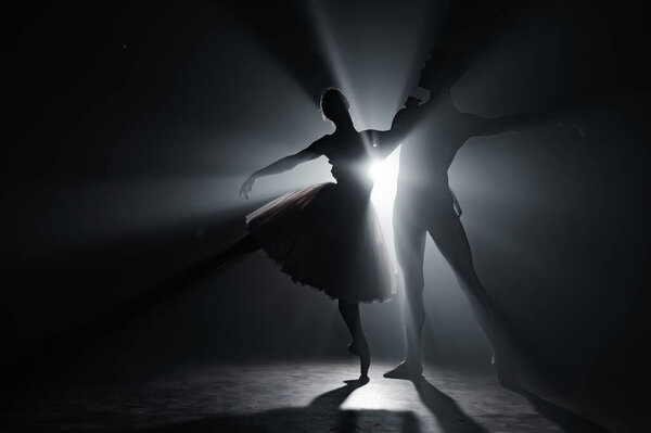 Изящная балерина и ее партнер-мужчина танцуют элементы классического или современного балета в темноте с подсветкой прожектора. Пара в дыму на черном фоне. Концепция искусства
.