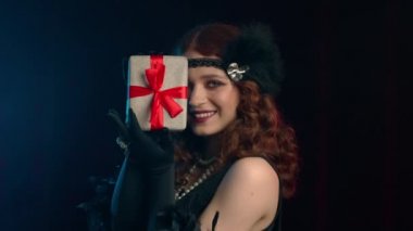 Kükreyen yirmili yıllarda giyinmiş neşeli, klasik bir kadın elinde kadife kaplı bir hediye kutusu tutuyor. O, hediye almaktan memnun. retro, parti, moda konsepti.