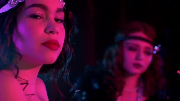Portrait of young flapper women dressed in style of Great Gatsby posing on dark background in pink neon light. Roaring twenties, retro, party, fashion concept — Stock Video