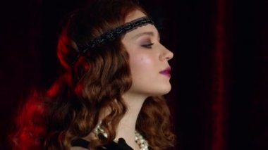 Great Gatsby dönemi tarzında giyinmiş eski moda kızıl saçlı kadının portresi. Flört ediyor ve bordo kadife arka planda poz veriyor. Vintage, flapper party, retro moda konsepti