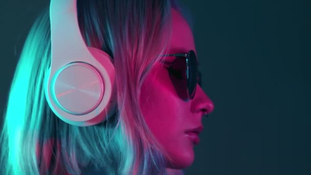 Underbar kvinna med färgat hår lyssna musik i hörlurar och sjunga med neon ljus bakgrund. Charmig hipster flicka dansar med solglasögon — Stockvideo