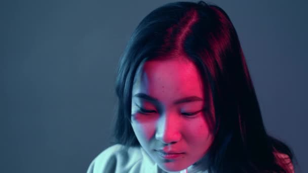 Junges hübsches Mädchen mit asiatischem Aussehen in neonrosa und blauem Licht in der Nacht. Seriöser trendiger Hipster-Teenager blickt in die Kamera — Stockvideo