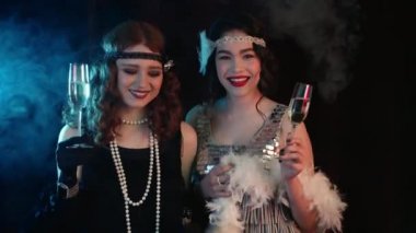 Kükreyen yirmili yaşlar tarzında giyinmiş, şampanya içen, yeni yılı ya da Cadılar Bayramı 'nı kutlayan çekici kadınlar. Klasik, retro parti, moda, kız arkadaş konsepti