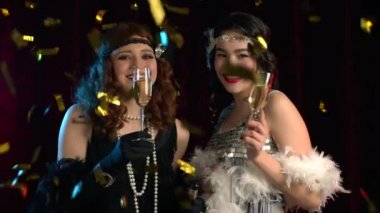 Kükreyen yirmili yaşlardaki güzel kadınlar konfeti yağmuru altında şampanya içerler. Klasik, retro parti, moda, kız arkadaş konsepti