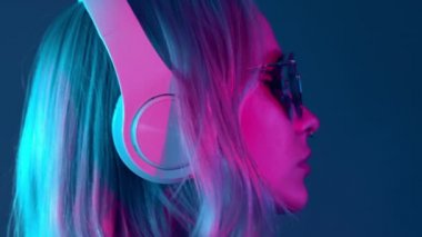 Boyalı saçları ve güneş gözlükleriyle kulaklıkla müzik dinleyen ve neon ışıklı arka planda şarkı söyleyen muhteşem bir bayan. Büyüleyici hippi kız gözleri kapalı dans ediyor..