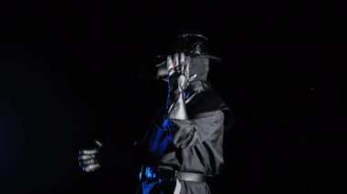 Veba doktoru kostümlü komik adamın komik bir mim görüntüsü. Karga benzeri maskeli ve elleri siyah arka planda yalnız dans ediyor. Ürkütücü maske, tarihi kostüm konsepti. Salgın