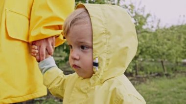  Sarı yağmurluk giymiş şirin bir çocuğun portresi. Çocuk annelerinin elini tutuyor. Aşk, ilgi, bağlılık, aile, çocuk konsepti.