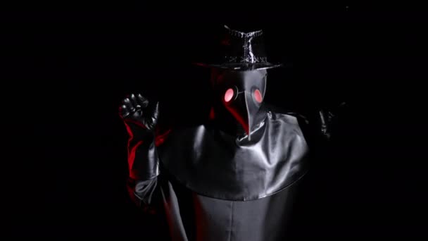 Plague doctor costume with crow-like mask makes funny gestures, as if pecking with a beak and flapping wings isolated on black background. Creepy mask, historical costume concept. Epidemic — Stock Video