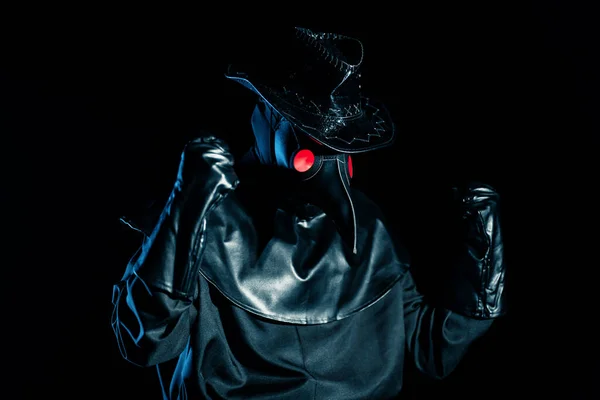 Man in plague doctor costume with crow-like mask showing yes winner gesture, rejoices isolated on black background. Creepy mask, historical costume concept. Epidemic
