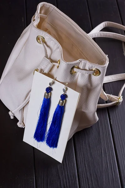 Pequeña mochila de mujer de cuero blanco y pendientes azules de hilo — Foto de Stock