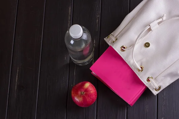 Белый кожаный рюкзак, розовая книга, бутылка воды — стоковое фото