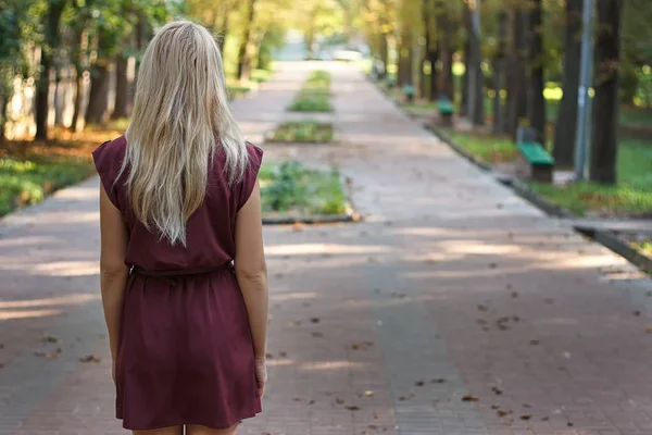 Chica rubia con el pelo largo en vestido de color burdeos de pie en el parque —  Fotos de Stock