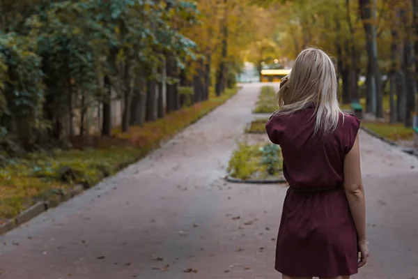 Chica rubia con el pelo largo en vestido de color burdeos de pie en el parque — Foto de Stock