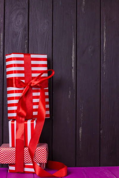 Slide of gifts in a red and white wrapper against a black wooden fence. — Stock Photo, Image